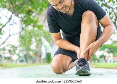 Young male in sports outfits black injured his ankle during exercise in the park. Low section of sports man suffering from flipped ankle while sitting on track during. Accident from exercise concept. - Powered by Shutterstock
