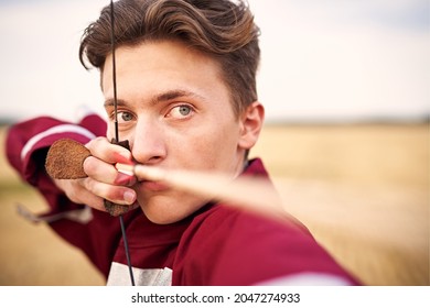 Young male sportsman targeting with bow in a traditional, medieval archer costume - Teenager archer practicing archery in nature - Field archery and recreation concept with a millennial boy