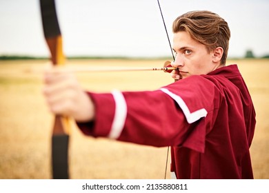 Young male sportsman targeting with bow in a traditional, medieval archer costume - Teenager archer practicing archery in nature - Field archery and recreation concept with a millennial boy