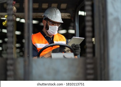 Young Male Staff Driving Forklift In Warehouse. Worker Man Wearing Face Mask Prevent Covid-19 Virus And Protective Hard Hat. Industrial And Industrial Workers Concept