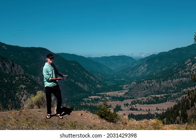 Young male standing high on a mountain overlooking the valley below on a clear summer day.