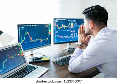 Young Male Stock Broker Praying For Good Fortune While Trading Online At Desk From Home