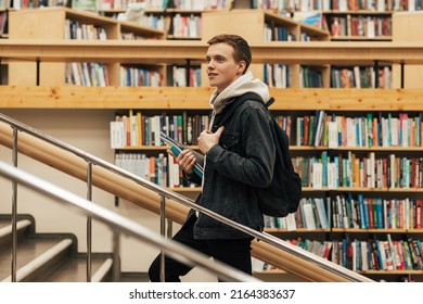 Young Male Student Going Up The Stairs In Library. Man With Textbooks In University Library.