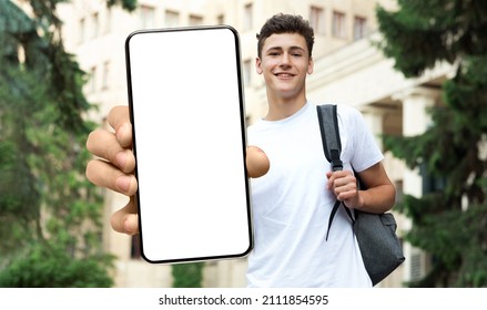 Young Male Student Showing Blank Mockup Screen Holding Big Phone In Hand Advertising Educational Application For Smartphone Standing Outdoors Near College Building, Showing Gadget Close Up To Camera