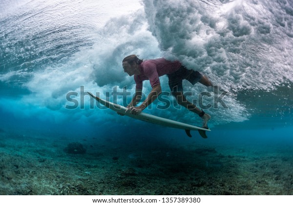 Young\
male surfer dives under the breaking ocean\
wave