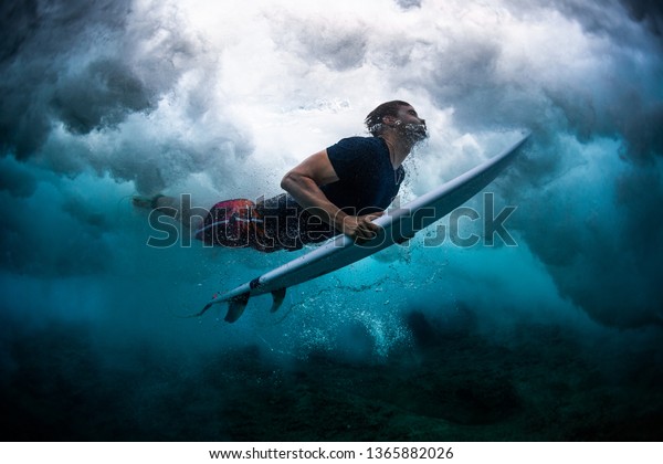 Young male surfer dives under the broken wave\
with his surfboard