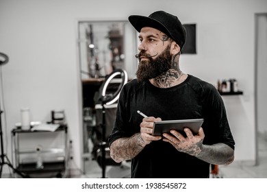 Young Male Tattoo Artist With Beard Holding Pencil And Sketch Looking Positive And Happy Standing And Smiling In Workshop Place