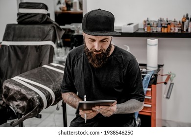 Young Male Tattoo Artist With Beard Holding Pencil And Sketch Looking Positive And Happy Standing And Smiling In Workshop Place.