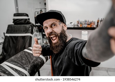 Young Male Tattoo Artist With Beard Taking Selfie And Looks Funny In Workshop Place Before Work.