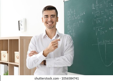 Young Male Teacher With Chalk Near Blackboard In Classroom