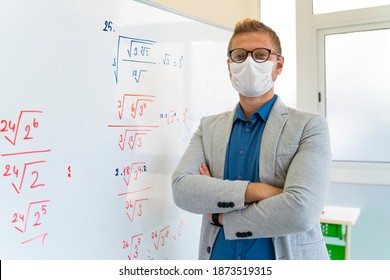 Young Male Teacher With Face Mask Writing On Whiteboard In Classroom 