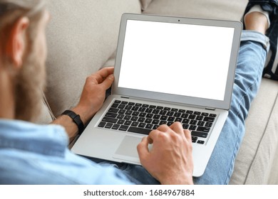 Young male tech user relaxing on sofa holding laptop computer mock up blank white screen. Man using modern notebook surfing internet, read news, distance online study work concept. Over shoulder view