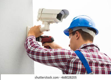 Young Male Technician Installing Camera On Wall With Screwdriver
