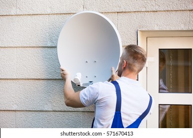 Young Male Technician Installing TV Satellite Dish To Wall