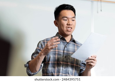 A young male teenage student is giving a presentation in front of the classroom, practicing his public speaking skills. He is reading off a paper script. - Powered by Shutterstock