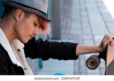 Young male teenager sitting sideways on city stairs holding a skateboard with a casual outfit, in a reflective and lonely mood, appearing lost in thought in an urban outdoor environment - Powered by Shutterstock - Get 15% off with code: PIKWIZARD15