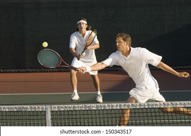 Young male tennis player hitting ball with doubles partner standing in background