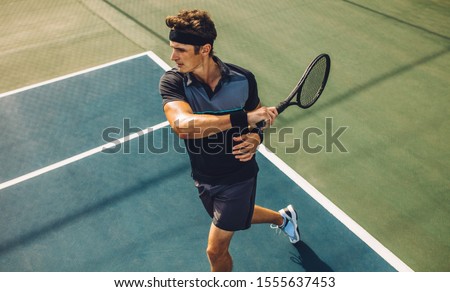 Young male tennis player hitting forehand during practice game on hard court. Pro tennis player playing tennis on court.