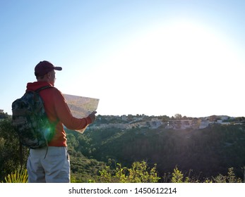 Young male tourist is considering a map, stands against the background of the city on the hill