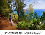 Young male tourist hiking on beautiful Pololu loop trail located near Kapaau, Hawaii, that features beautiful wild flowers and stunning views to the Pololu Valley. Big Island, Hawaii.