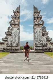 Young Male Tourist Wearing A Traditional Balinese Sarong Walking In Front Of Gates Of Heaven Temple In North Bali Indonesia