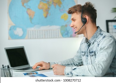 Young Male Travel Agent Consultant In Tour Agency Using Headset