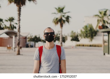 Young Male Traveler With Backpack And In Sun Glasses Wearing Black Protective Mask. Covid 19 Or Coronavirus Pandemic Concept. Man In A Dust Protection Reusable  Mask