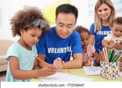 Junge männliche Freiwillige zeichnen mit kleinen Kindern am Tisch. Konzept der Freiwilligentätigkeit im Ausland