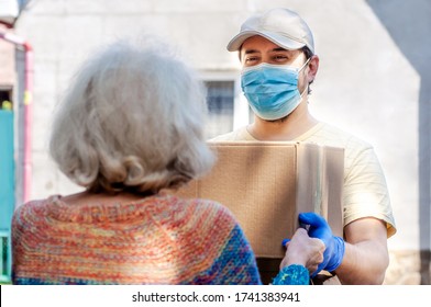 Young male volunteer in mask gives an elderly woman boxes with food near her house. Son man helps a single elderly mother. Family support, caring. Quarantined, isolated. Coronavirus covid-19. Donation