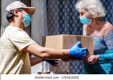 Young male volunteer in mask gives an elderly woman boxes with food near her house. Son helps a single elderly mother. Family support, caring. Quarantined, isolated. Coronavirus covid-19. Donation - Shutterstock ID 1761616103