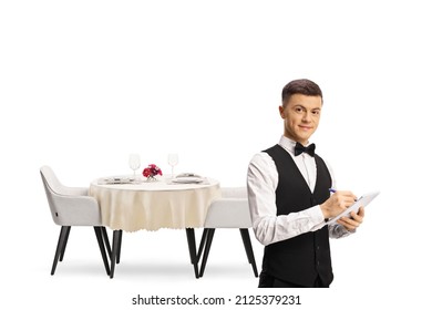 Young Male Waiter With A Bow Tie In Front Of A Restaurant Table Isolated On White Background