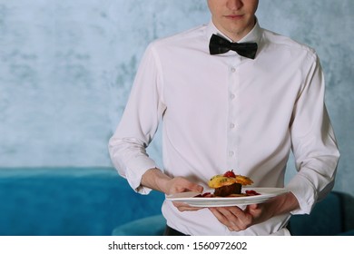 A Young Male Waiter Holds In His Hands A Cooked Dish From The Restaurant Menu. The Concept Of The Restaurant Business. Photo Without A Face, Only Hands.