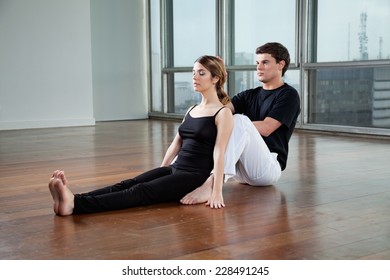 Young Male Yoga Instructor Helping Woman With A Pose At Gym