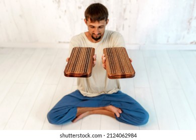 A Young Male Yogi Sits In The Lotus Position. In Each Hand, A Man Holds A Wooden Sadhu Board With Nails.