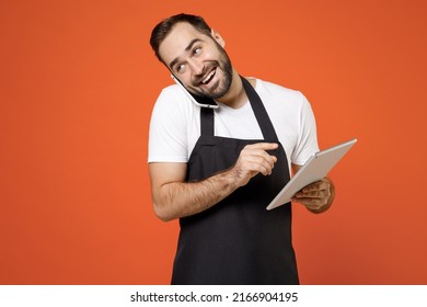 Young man 20s barista bartender barman employee wear black apron white t-shirt work in coffee shop use tablet pc computer talk by mobile cell phone isolated on orange background Small business startup - Powered by Shutterstock