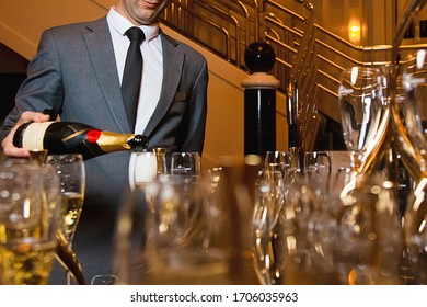 A Young Man Of 25-30 Years Old Pours Champagne Into Glasses At A Buffet Table