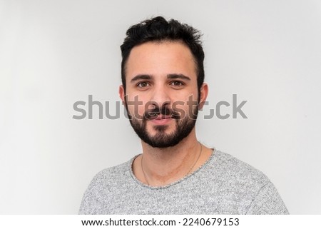 a young man 25-30 years old with a beard on a white background looks directly into the camera.