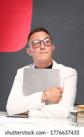 A Young Man Of 30-35 Years Old In A White Jacket, Black Turtleneck, Glasses And A Short Haircut Holds An Empty Sign In His Hands. Template For Design, Mockup.