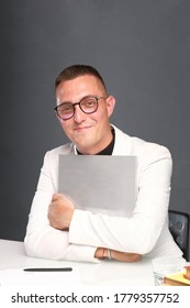 A Young Man Of 30-35 Years Old In A White Jacket, Black Turtleneck, Glasses And A Short Haircut Holds An Empty Sign In His Hands. Template For Design, Mockup.