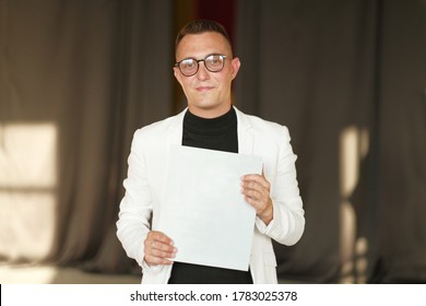 A Young Man Of 30-35 Years Old In A White Jacket, Black Turtleneck, Glasses And A Short Haircut Holds An Empty Sign In His Hands. Template For Design, Mockup.