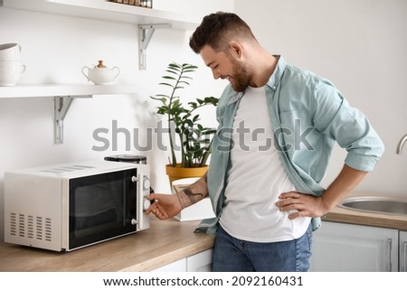 Young man adjusting microwave oven in kitchen