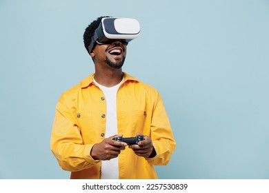 Young man of African American ethnicity 20s wear yellow shirt hold in hand play pc game with joystick console watching in vr headset pc gadget isolated on plain pastel light blue background studio. - Powered by Shutterstock