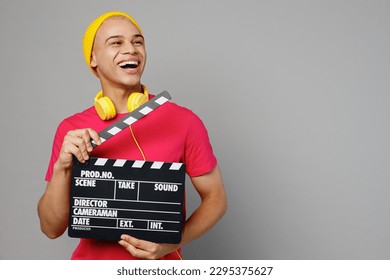 Young man of African American ethnicity 20s wear pink t-shirt yellow hat headphones holding classic black film making clapperboard look aside on area mock up isolated on plain grey background studio - Powered by Shutterstock