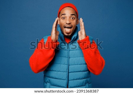 Young man of African American ethnicity he wear padded vest red hat scream sharing hot news about sales discount with hands near mouth isolated on plain dark royal navy blue background studio portrait
