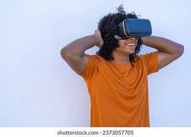 A young man with afro hair enjoying virtual reality glasses wearing a bright orange t-shirt on a white background. - Powered by Shutterstock