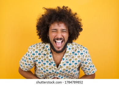 Young man with afro hair over  wearing hawaiian shirt standing over yellow background  smiling and laughing hard out loud because funny crazy joke with hands on body. - Shutterstock ID 1784789852