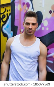 Young Man Against Bright Colored Graffiti Wall Wearing White Tanktop