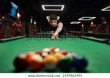 Young man aiming with billiards cue