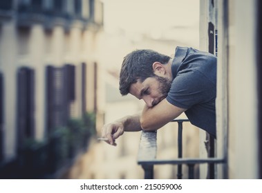 Young Man Alone Outside At House Balcony Terrace Smoking Depressed, Destroyed, Wasted And Sad Suffering Emotional Crisis And Depression On Urban Background 