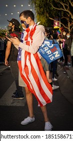 Young man with American flag holding a Joe Biden and Kamala Harris election 2020 flag in his hand with mask on celebrating election day in Los Angeles 2020￼￼